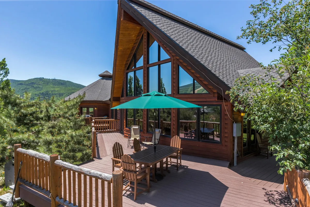 A sun-dappled wooden deck surrounded by lush trees, featuring a green umbrella and outdoor dining area. The deck’s elevation and proximity to nature are evident, reinforcing the lodge's inviting outdoor spaces.