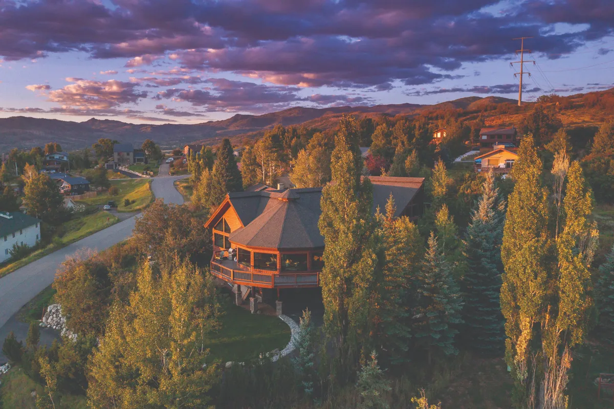 A broad view of the property’s unique architecture with a road leading up, surrounded by trees and a grand mountain backdrop. The perspective emphasizes both accessibility and the dramatic landscape.