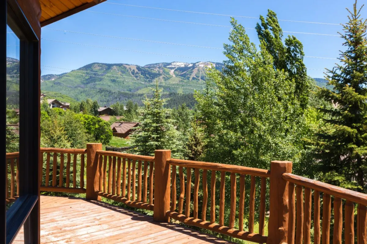 A serene view from the deck, featuring a sturdy railing, glimpses of nearby trees, and a sweeping mountain vista. The setting is peaceful, ideal for morning coffee or stargazing, and emphasizes the value of exclusive outdoor spaces.
