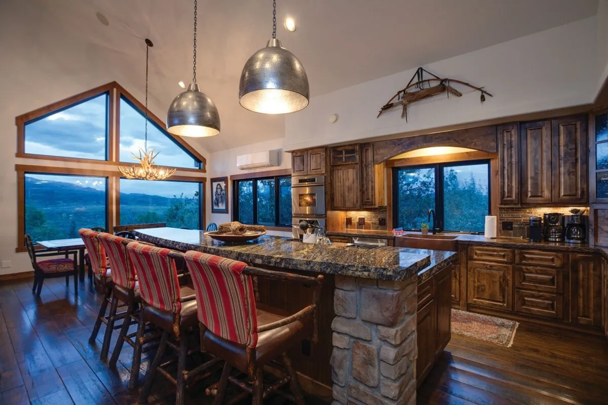 An expansive kitchen island surrounded by panoramic windows, stylish pendant lights overhead, and an airy, open-concept layout. The scene suggests plenty of space for meal prep and guest interaction, with natural light streaming in.