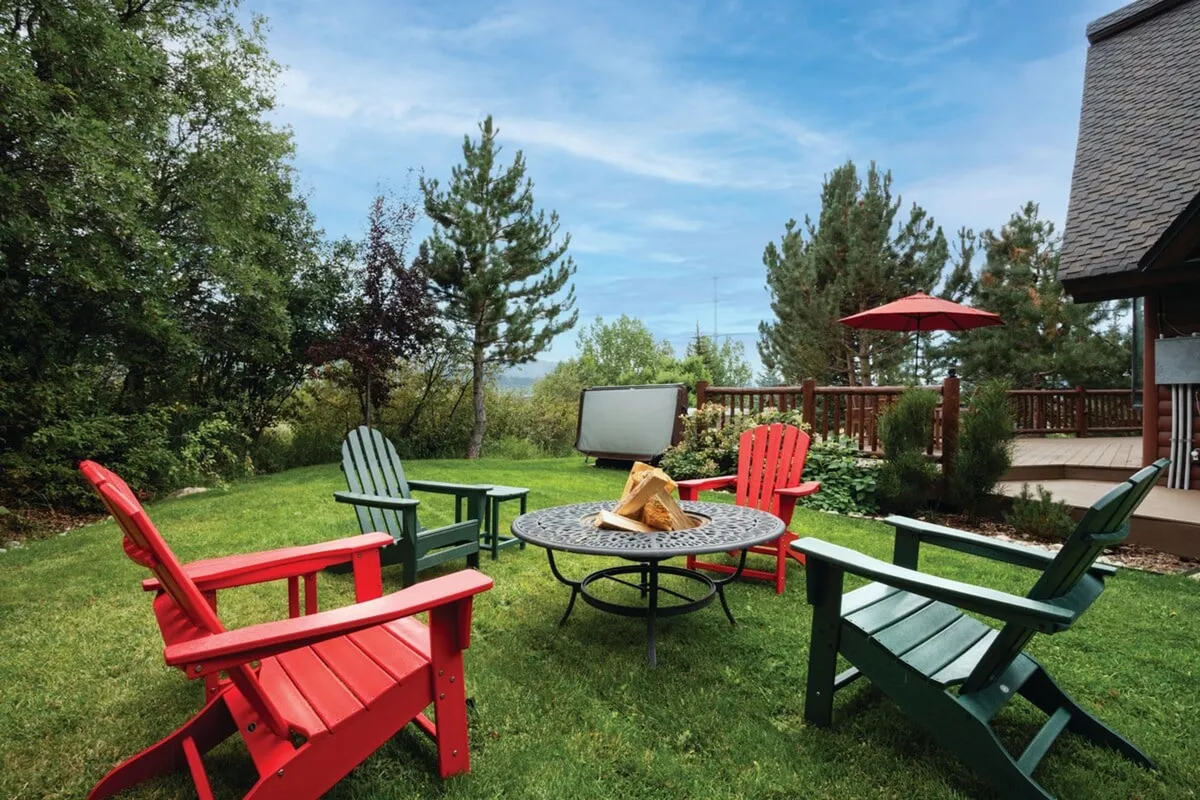 A cozy exterior scene featuring vibrant red and green Adirondack chairs gathered around a fire pit on a wooden deck. The area is clearly designed for socializing and enjoying the outdoors, with the fire pit enhancing comfort and the cheerful atmosphere.