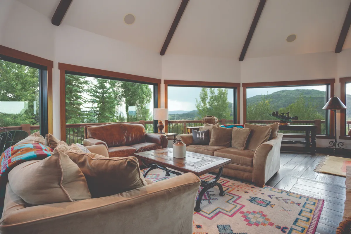 A comfortable lounge area featuring plush sofas, a decorative rug, and a wooden coffee table—all oriented to enjoy magnificent views through vast floor-to-ceiling windows. The room exudes a warm, inviting atmosphere perfect for relaxing or socializing.